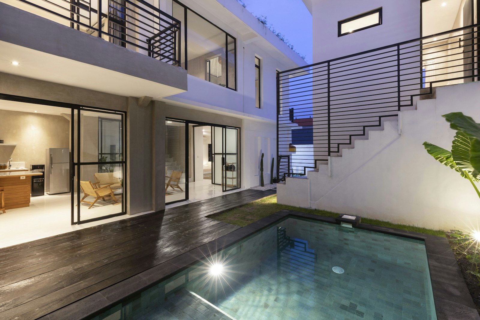 Piscine en pierre verte et terrasse en bois sombre de la Villa Leelu, baies vitrées éclairées en début de soirée